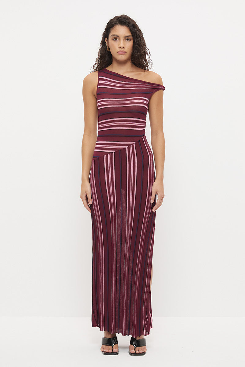 Woman wearing a fully fashioned fine knit one-shoulder maxi dress in a multi-directional stripe with a twisted off-shoulder strap, angled dropped waist, and flared skirt with side split.