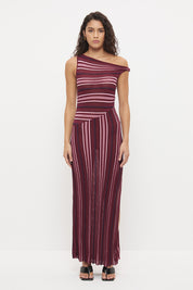 Woman wearing a fully fashioned fine knit one-shoulder maxi dress in a multi-directional stripe with a twisted off-shoulder strap, angled dropped waist, and flared skirt with side split.