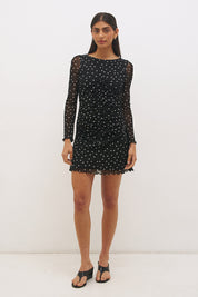 Woman wearing a printed polka dot mesh long sleeve mini dress with a fit-and-flare silhouette, boat neckline, sheer sleeves, and lettuce hem detail.