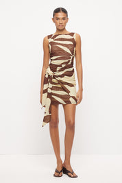 Sleeveless fitted mini dress with boat neckline, side ruching and sarong tie overlay in exclusive handcrafted print