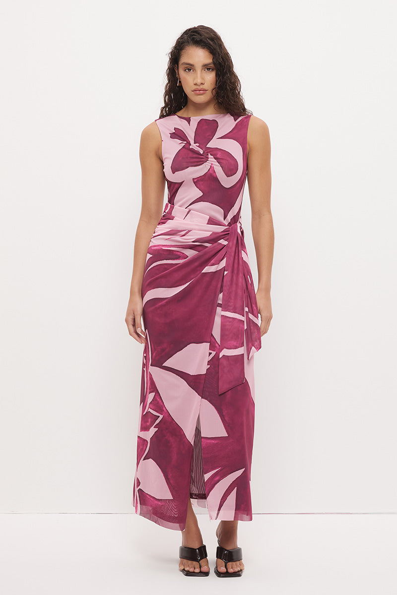 Woman wearing a sleeveless maxi dress with an exclusive placement print, sarong-style wrap skirt overlay, ruched asymmetric waistband, and boat neckline in a softly A-lined silhouette