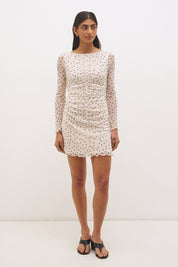 Woman wearing a printed polka dot mesh long sleeve mini dress with a fit-and-flare silhouette, boat neckline, sheer sleeves, and lettuce hem detail.