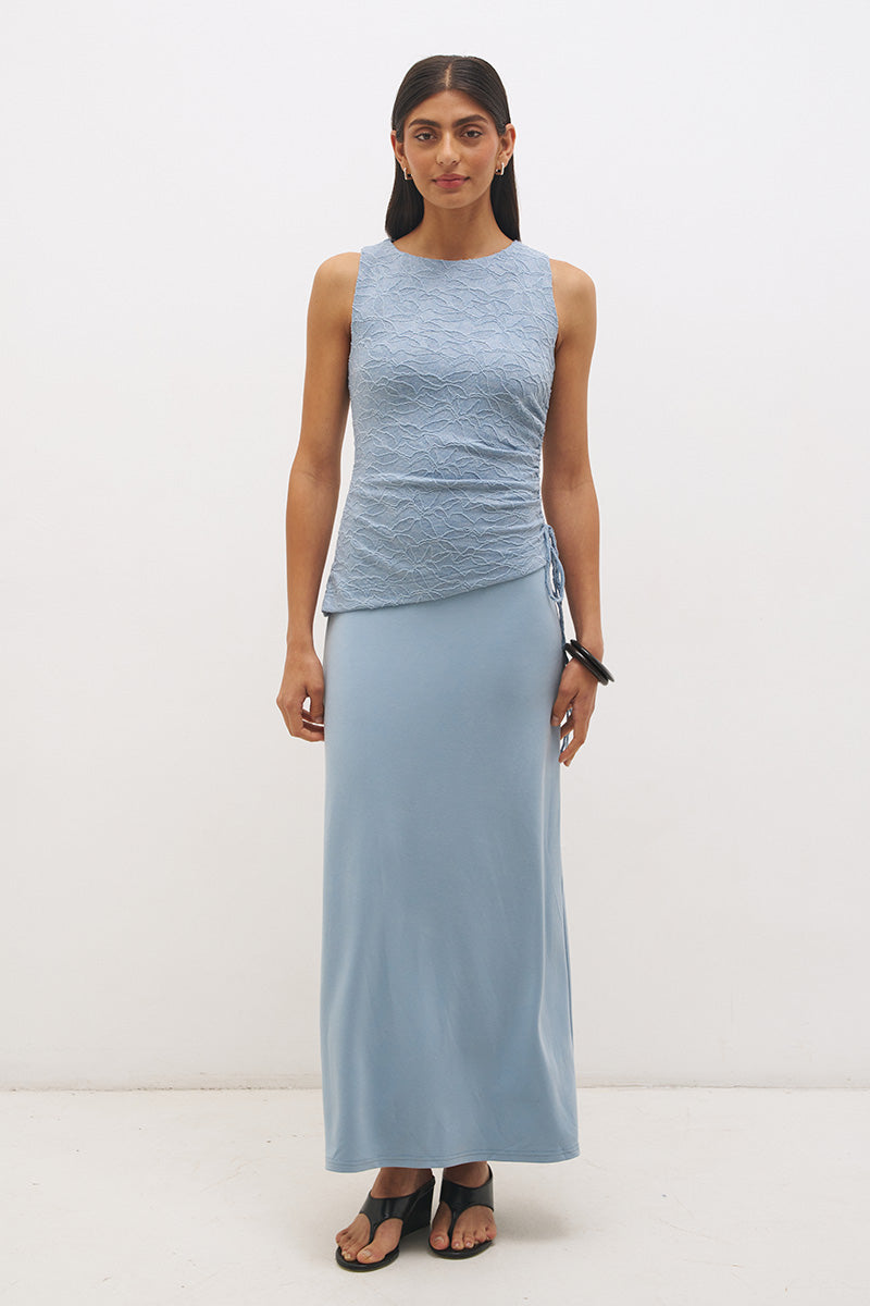 Woman wearing a sleeveless maxi dress with a textured lace bodice overlay, sunray ruching, boat neckline, and a contrast smooth A-line modal skirt in a fit-and-flare silhouette.