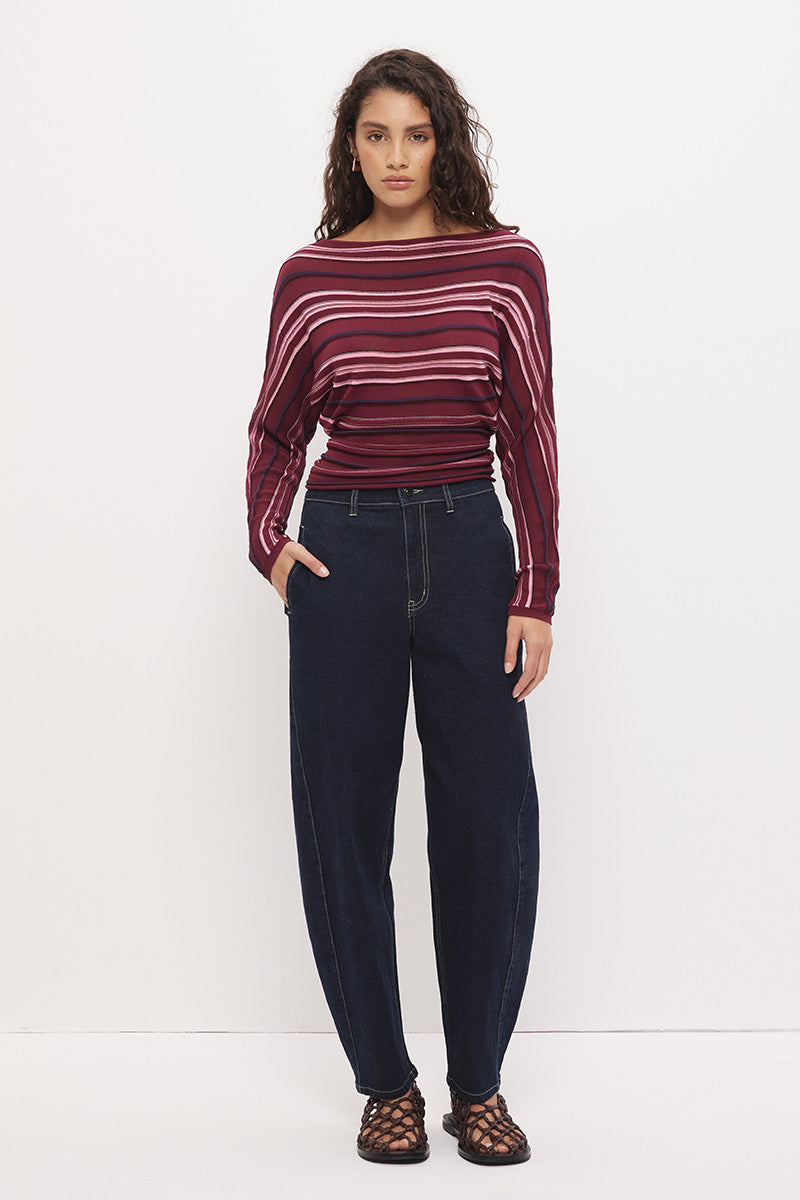 Woman wearing a fully fashioned fine knit long sleeve top in a horizontal multi-stripe with a boat neckline, wide batwing sleeves, dropped shoulders, and soft waistline gathering.