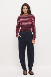 Woman wearing a fully fashioned fine knit long sleeve top in a horizontal multi-stripe with a boat neckline, wide batwing sleeves, dropped shoulders, and soft waistline gathering.