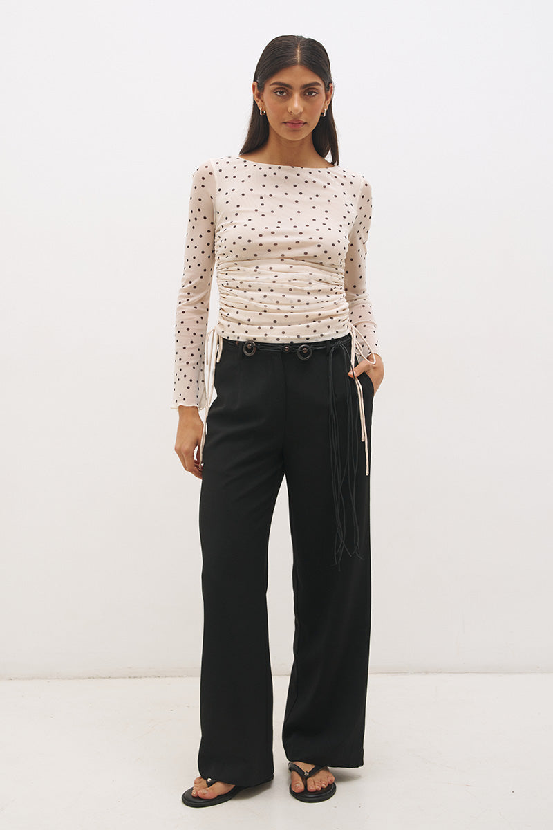 Woman wearing a printed polka dot mesh long sleeve longline top with a boat neckline, sheer sleeves, lettuce hem cuffs, and a drawcord waist detail.