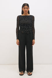 Woman wearing a printed polka dot mesh long sleeve longline top with a boat neckline, sheer sleeves, lettuce hem cuffs, and a drawcord waist detail.