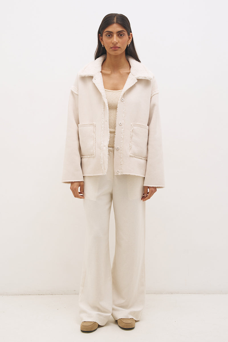 Woman wearing reversible suedette shearling oversized jacket with convertible collar, exposed seams, and raw cut hem details