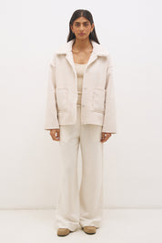Woman wearing reversible suedette shearling oversized jacket with convertible collar, exposed seams, and raw cut hem details