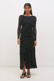 Woman wearing a printed polka dot mesh long sleeve midi dress in a column silhouette, with a boat neckline, sheer sleeves, bodice ruching, and a curved side frill split detail.
