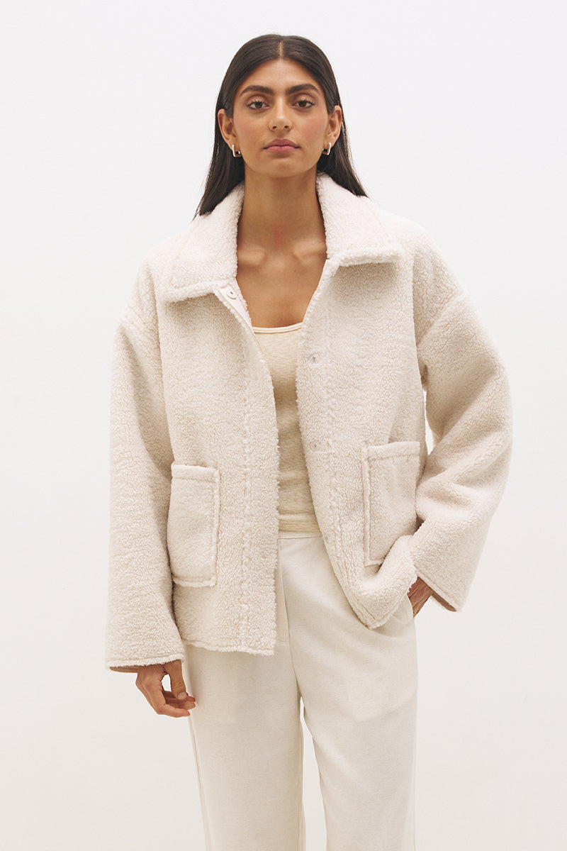 Woman wearing reversible suedette shearling oversized jacket with convertible collar, exposed seams, and raw cut hem details