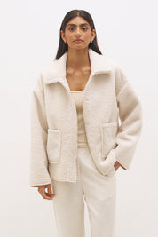 Woman wearing reversible suedette shearling oversized jacket with convertible collar, exposed seams, and raw cut hem details
