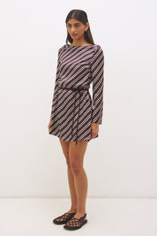 Woman wearing an asymmetric stripe satin mini dress with boat neckline, flared sleeves, flared hem, and removable waist tie