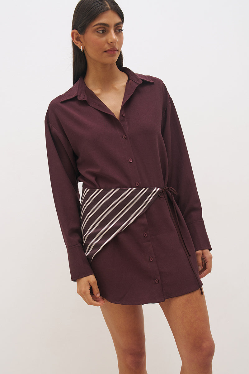 Woman wearing a satin-backed linen blend shirt dress with relaxed fit, collar neckline, curved hem, long sleeves, and removable scarf waist tie