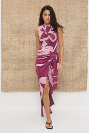Woman wearing a sleeveless maxi dress with an exclusive placement print, sarong-style wrap skirt overlay, ruched asymmetric waistband, and boat neckline in a softly A-lined silhouette