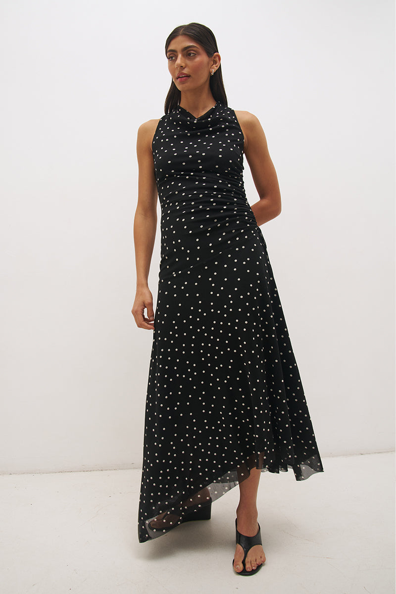 Woman wearing a printed polka dot mesh sleeveless midi dress with a draped cowl neckline, fit-and-flare silhouette, ruched drawcord waist, and asymmetric hi-lo raw-cut hem.