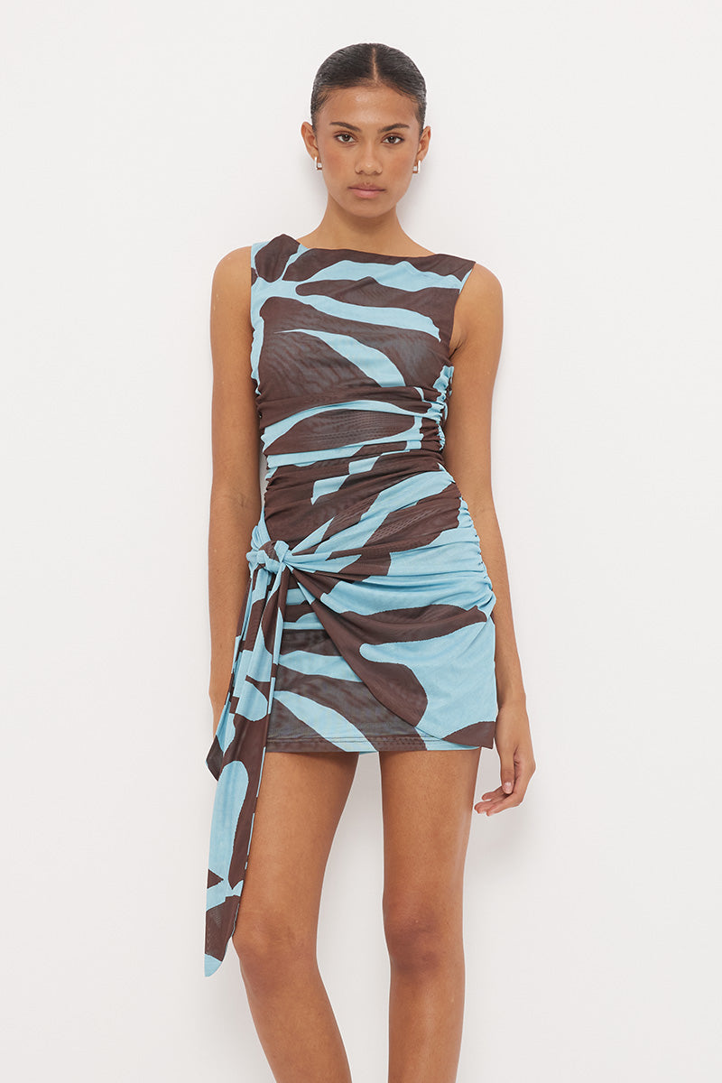 Sleeveless fitted mini dress with boat neckline, side ruching and sarong tie overlay in exclusive handcrafted print