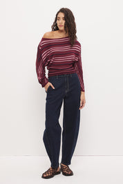 Woman wearing a fully fashioned fine knit long sleeve top in a horizontal multi-stripe with a boat neckline, wide batwing sleeves, dropped shoulders, and soft waistline gathering.
