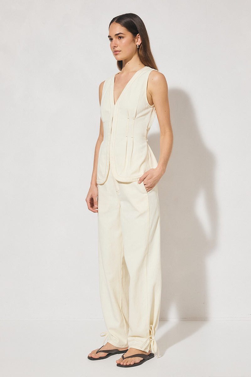 Sleeveless denim longline vest top with V neckline, pintucked waist, back tie, curved front hem, banded edges, and contrast topstitching