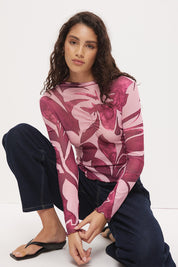 Woman wearing a semi-sheer long sleeve top in stretch ribbed mesh with an exclusive placement print, funnel neckline, centre front chest ruching, and lettuce hem finishes.
