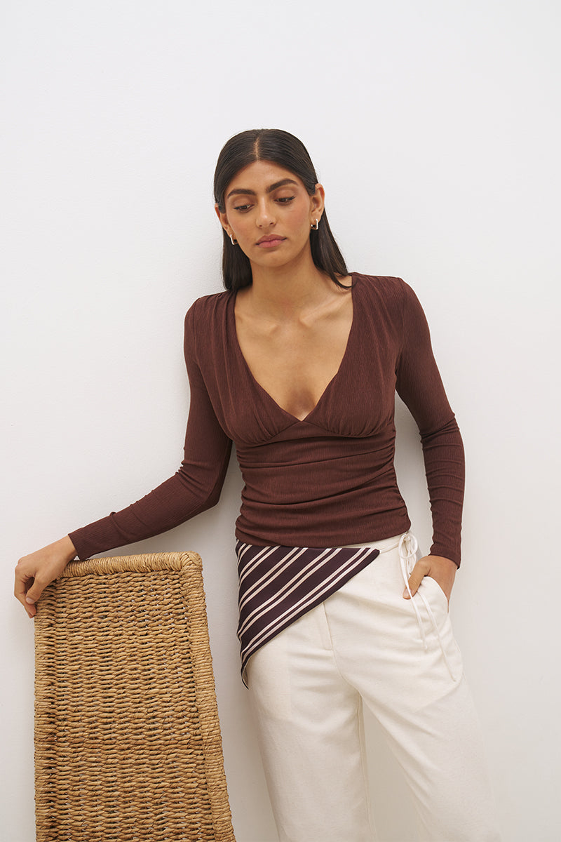 Woman wearing a textured cupro jersey long sleeve top with plunging V neckline, gathered bust detail, empire waist silhouette, and skimming fit