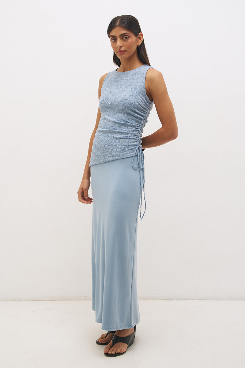 Woman wearing a sleeveless maxi dress with a textured lace bodice overlay, sunray ruching, boat neckline, and a contrast smooth A-line modal skirt in a fit-and-flare silhouette.
