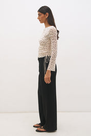 Woman wearing a printed polka dot mesh long sleeve longline top with a boat neckline, sheer sleeves, lettuce hem cuffs, and a drawcord waist detail.
