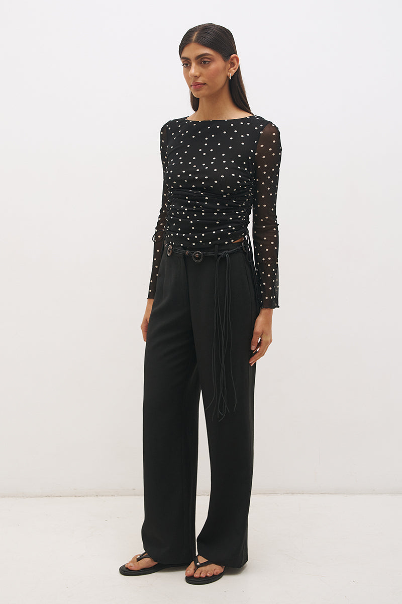 Woman wearing a printed polka dot mesh long sleeve longline top with a boat neckline, sheer sleeves, lettuce hem cuffs, and a drawcord waist detail.