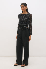 Woman wearing a printed polka dot mesh long sleeve longline top with a boat neckline, sheer sleeves, lettuce hem cuffs, and a drawcord waist detail.