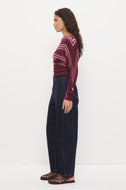 Woman wearing a fully fashioned fine knit long sleeve top in a horizontal multi-stripe with a boat neckline, wide batwing sleeves, dropped shoulders, and soft waistline gathering.