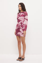 Woman wearing a long sleeve bodycon mini dress in stretch ribbed mesh with an exclusive placement print, boat neckline, curved ruched waist seams, and fitted semi-sheer sleeves.