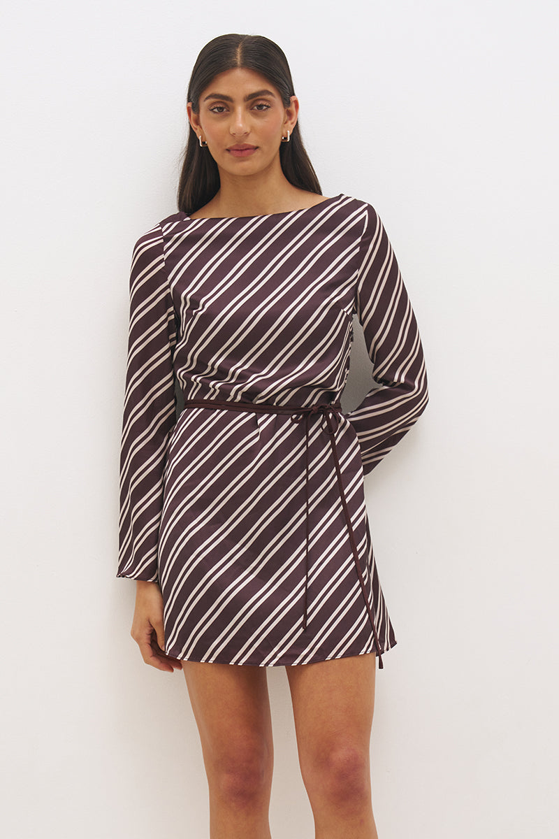 Woman wearing an asymmetric stripe satin mini dress with boat neckline, flared sleeves, flared hem, and removable waist tie