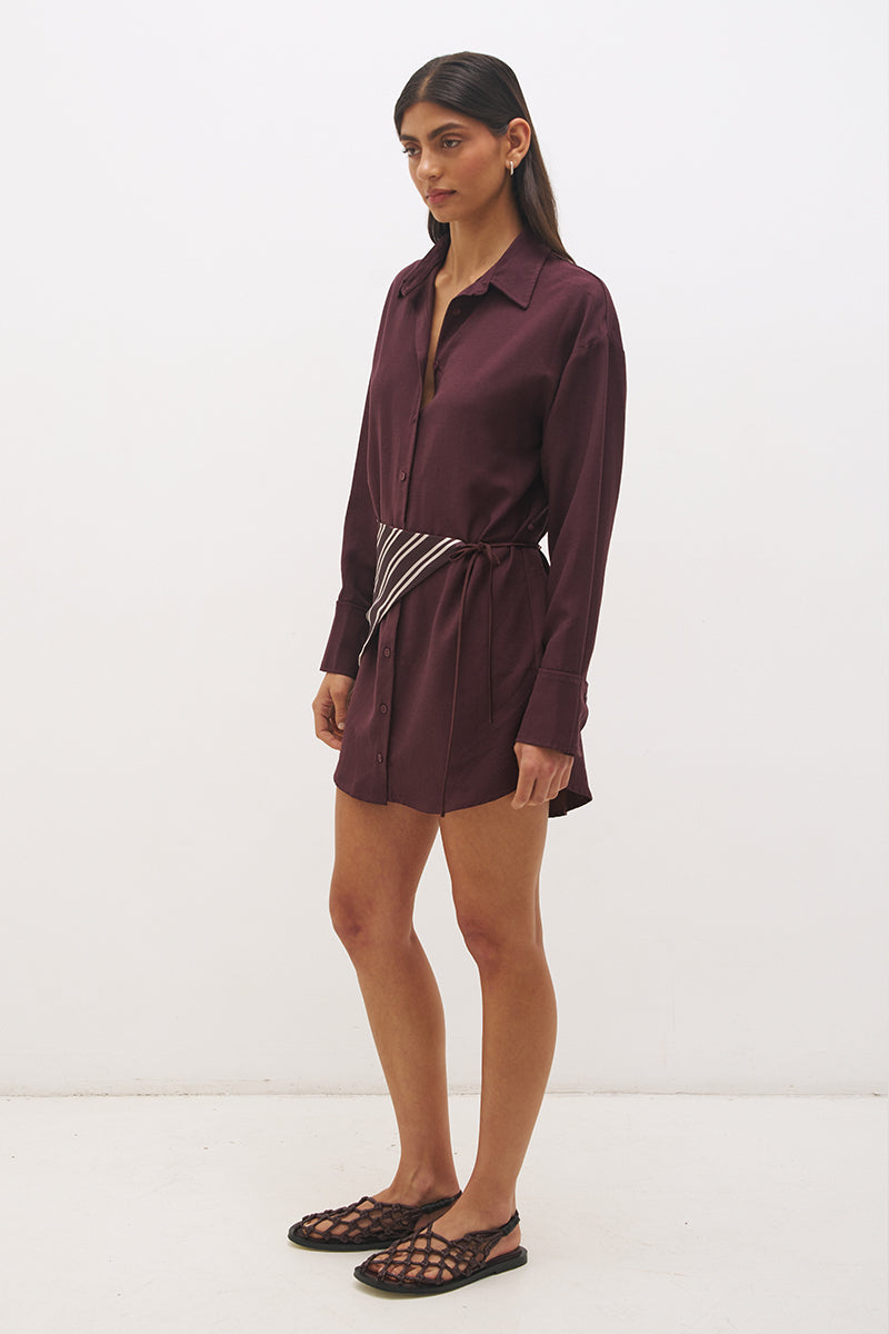 Woman wearing a satin-backed linen blend shirt dress with relaxed fit, collar neckline, curved hem, long sleeves, and removable scarf waist tie