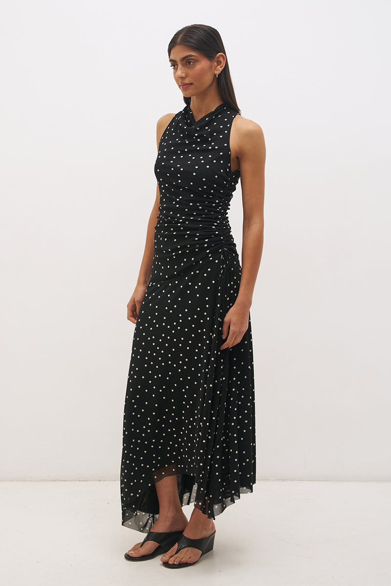 Woman wearing a printed polka dot mesh sleeveless midi dress with a draped cowl neckline, fit-and-flare silhouette, ruched drawcord waist, and asymmetric hi-lo raw-cut hem.