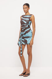 Sleeveless fitted mini dress with boat neckline, side ruching and sarong tie overlay in exclusive handcrafted print