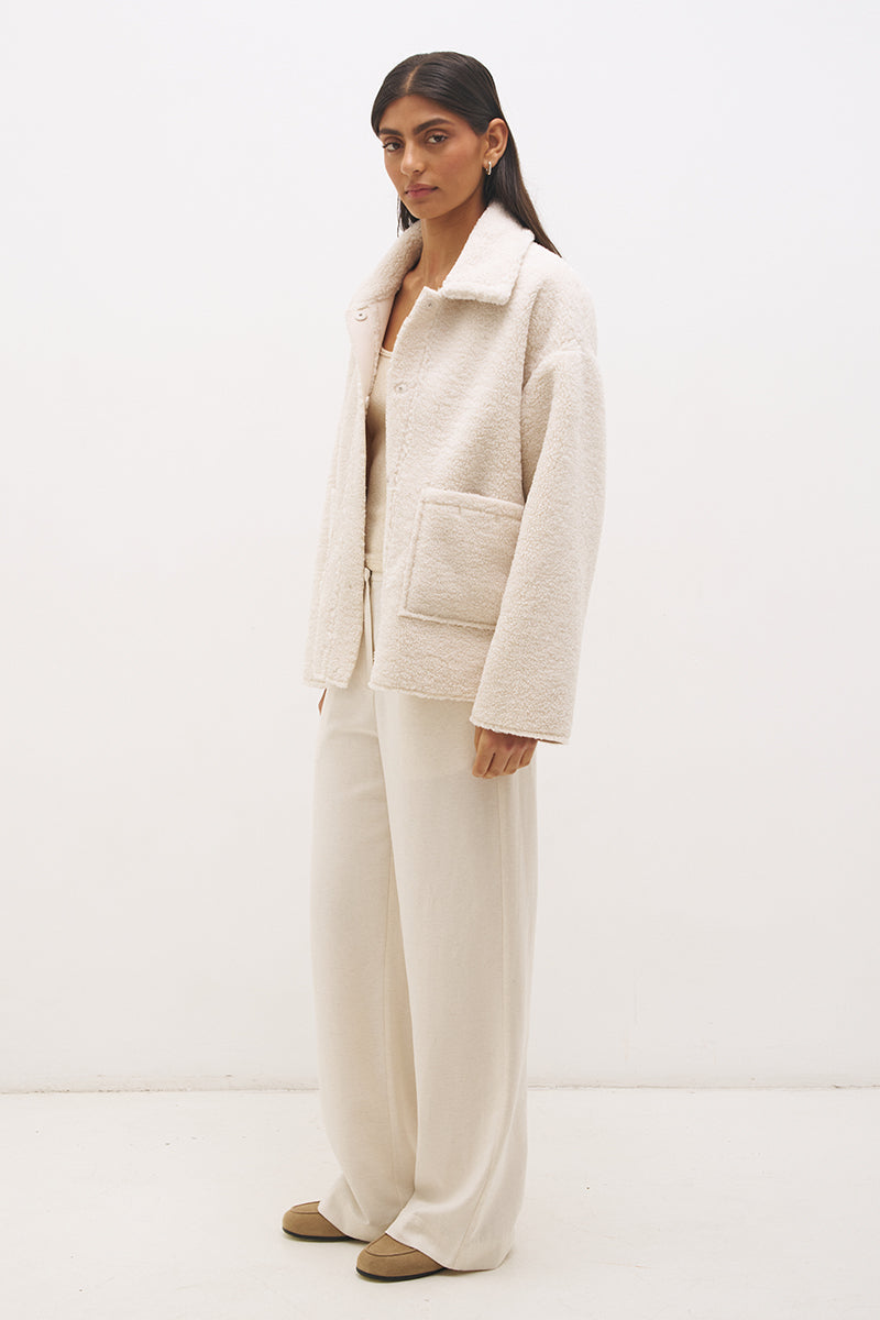 Woman wearing reversible suedette shearling oversized jacket with convertible collar, exposed seams, and raw cut hem details
