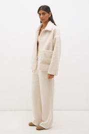 Woman wearing reversible suedette shearling oversized jacket with convertible collar, exposed seams, and raw cut hem details