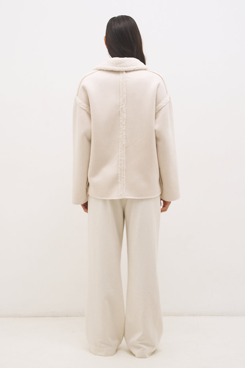 Woman wearing reversible suedette shearling oversized jacket with convertible collar, exposed seams, and raw cut hem details