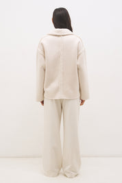 Woman wearing reversible suedette shearling oversized jacket with convertible collar, exposed seams, and raw cut hem details