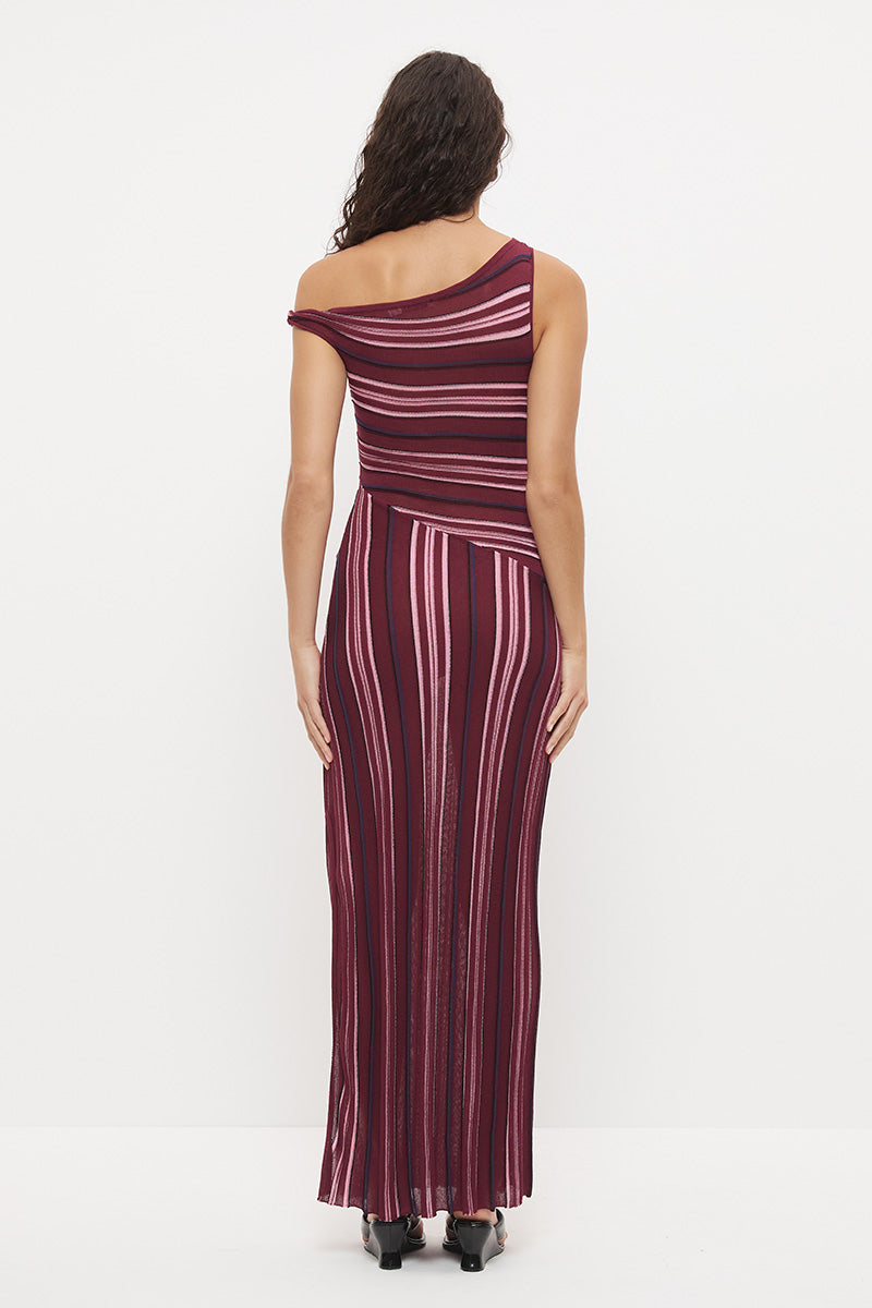 Woman wearing a fully fashioned fine knit one-shoulder maxi dress in a multi-directional stripe with a twisted off-shoulder strap, angled dropped waist, and flared skirt with side split.