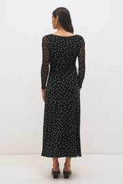 Woman wearing a printed polka dot mesh long sleeve midi dress in a column silhouette, with a boat neckline, sheer sleeves, bodice ruching, and a curved side frill split detail.