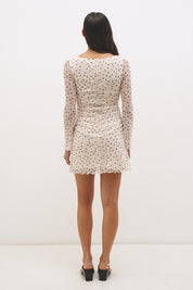 Woman wearing a printed polka dot mesh long sleeve mini dress with a fit-and-flare silhouette, boat neckline, sheer sleeves, and lettuce hem detail.