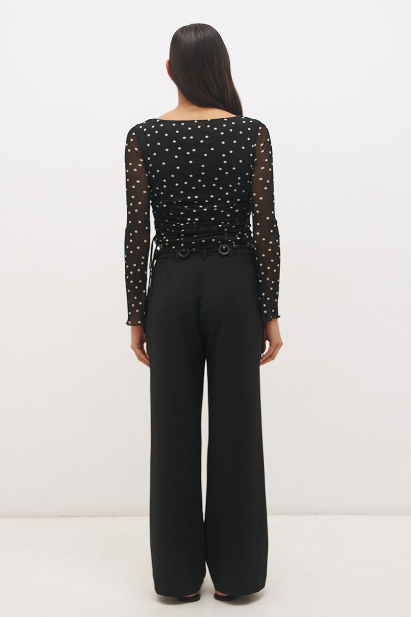 Woman wearing a printed polka dot mesh long sleeve longline top with a boat neckline, sheer sleeves, lettuce hem cuffs, and a drawcord waist detail.