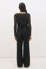 Woman wearing a printed polka dot mesh long sleeve longline top with a boat neckline, sheer sleeves, lettuce hem cuffs, and a drawcord waist detail.