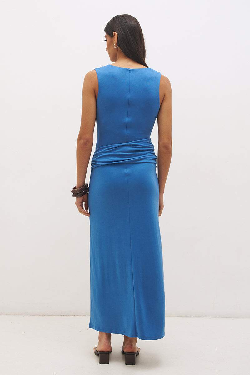 Woman wearing sleeveless jersey knit maxi dress with cowl neckline, spiral ring waist detail, cascading ruching, and fit-and-flare silhouette