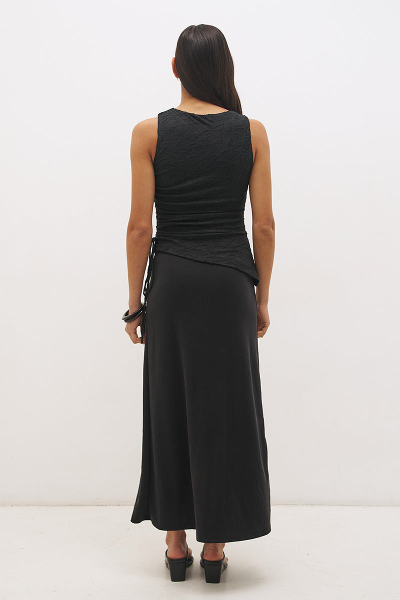Woman wearing a sleeveless maxi dress with a textured lace bodice overlay, sunray ruching, boat neckline, and a contrast smooth A-line modal skirt in a fit-and-flare silhouette.