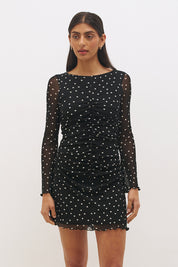 Woman wearing a printed polka dot mesh long sleeve mini dress with a fit-and-flare silhouette, boat neckline, sheer sleeves, and lettuce hem detail.