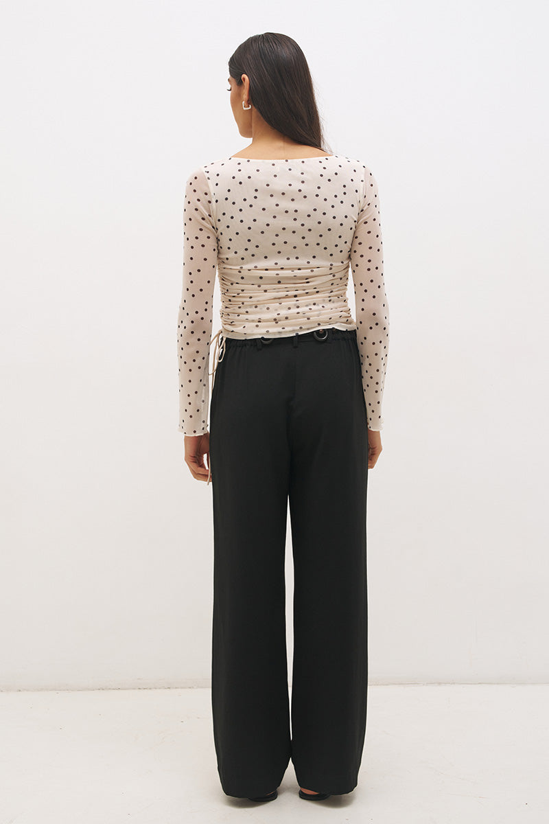 Woman wearing a printed polka dot mesh long sleeve longline top with a boat neckline, sheer sleeves, lettuce hem cuffs, and a drawcord waist detail.