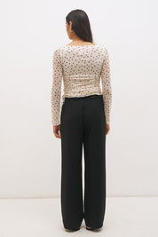 Woman wearing a printed polka dot mesh long sleeve longline top with a boat neckline, sheer sleeves, lettuce hem cuffs, and a drawcord waist detail.