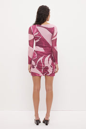 Woman wearing a long sleeve bodycon mini dress in stretch ribbed mesh with an exclusive placement print, boat neckline, curved ruched waist seams, and fitted semi-sheer sleeves.